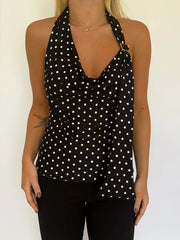 Black halter top with white polka dots worn by a person on a plain background