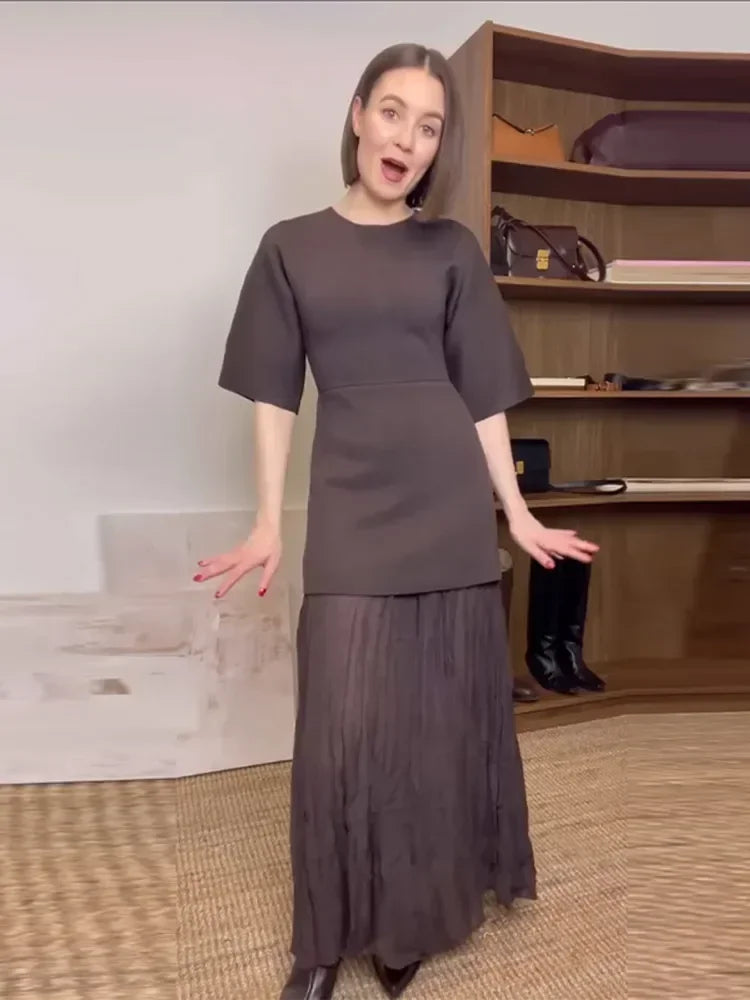 Woman wearing a gray outfit standing in front of a shoe rack with shoes on shelves.