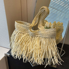Woven bag with fringe and tulips on a stand against a neutral background