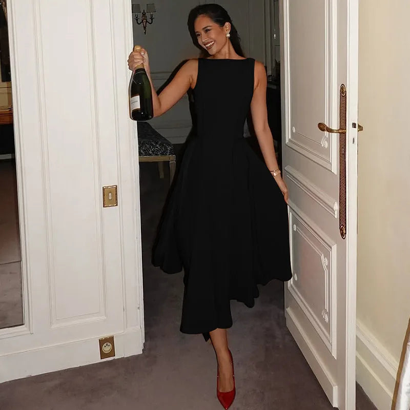 Woman in a black dress holding a bottle of champagne in a doorway.