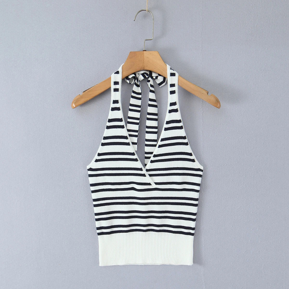 Black and white striped halter top on a wooden hanger against a gray background