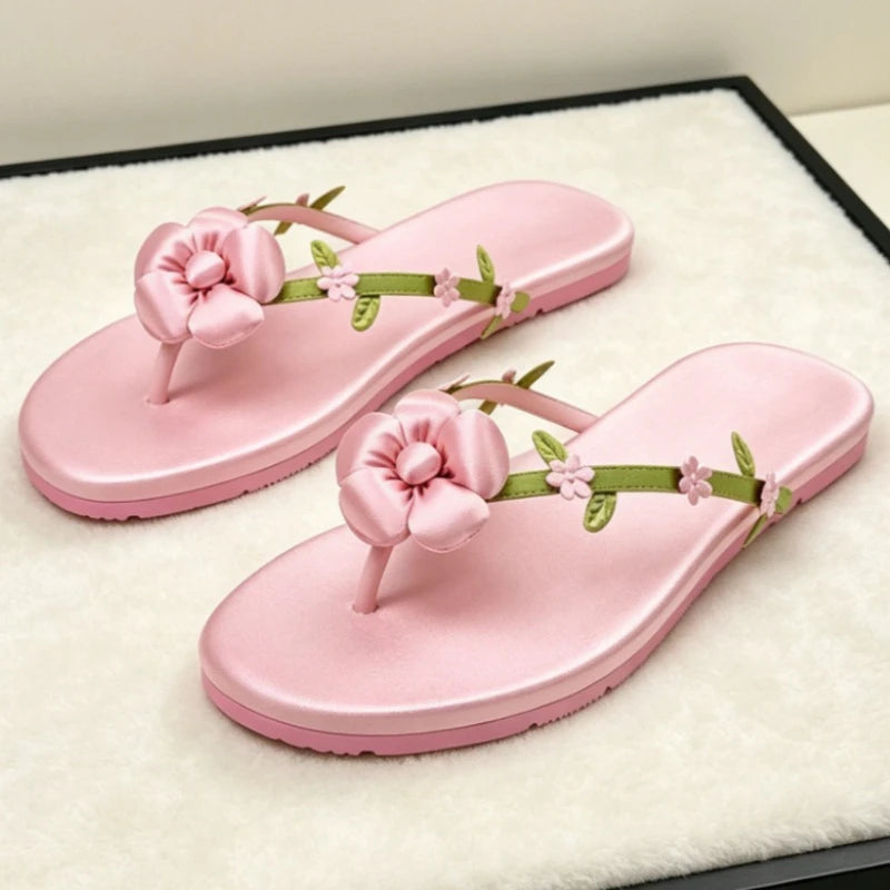 Pink satin flip flops with a large pink flower and green leaf accents.