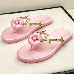 Pink satin flip flops with a large pink flower and green leaf accents.