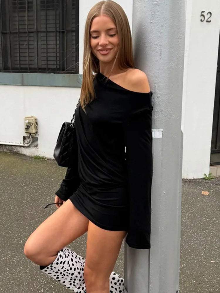 Black one shoulder mini dress with draped detail leaning on pole