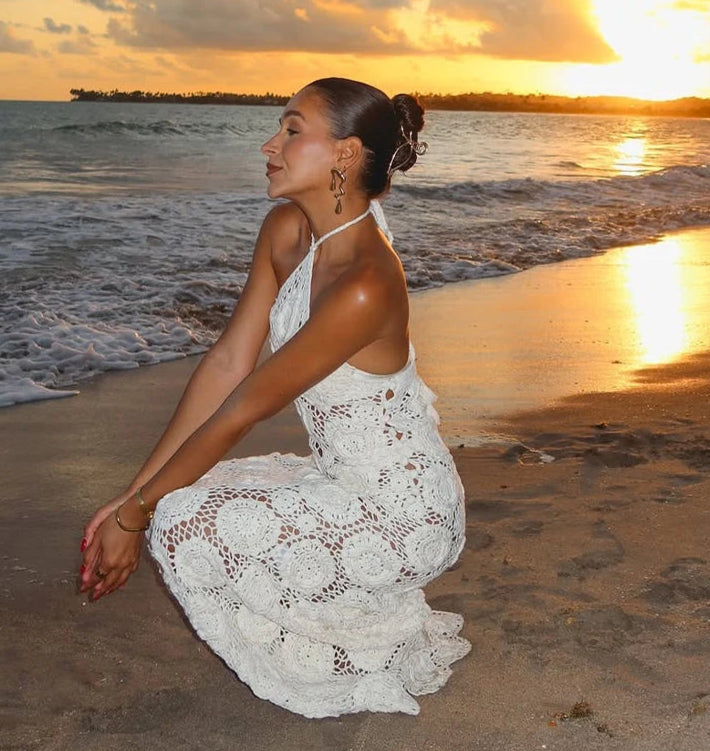 Woman in a white dress sitting on a beach at sunset