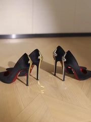 Black high-heeled shoes with decorative straps on a wooden floor.