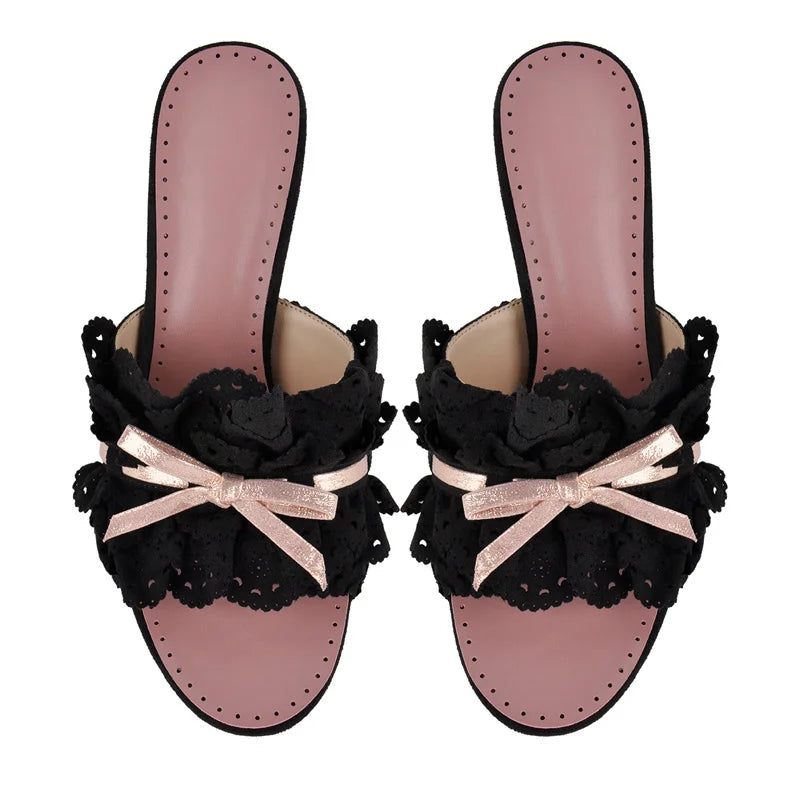 Pair of black eyelet lace slide mules with pink insoles and bows
