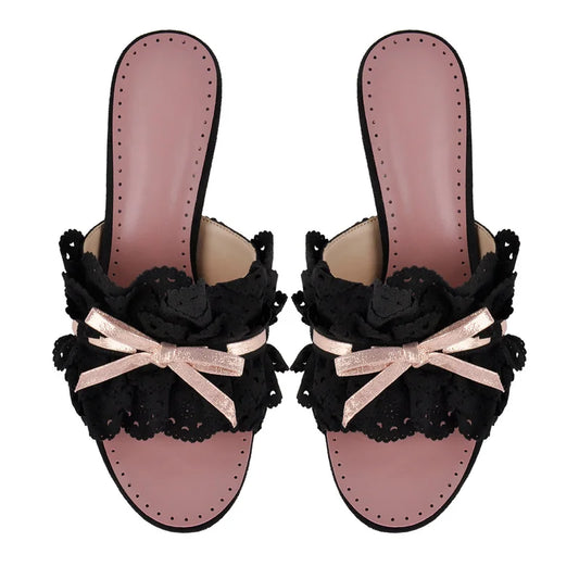 Pair of black eyelet lace slide mules with pink insoles and bows