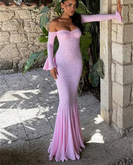 Woman in a pink off-shoulder dress standing against a stone wall with plants.