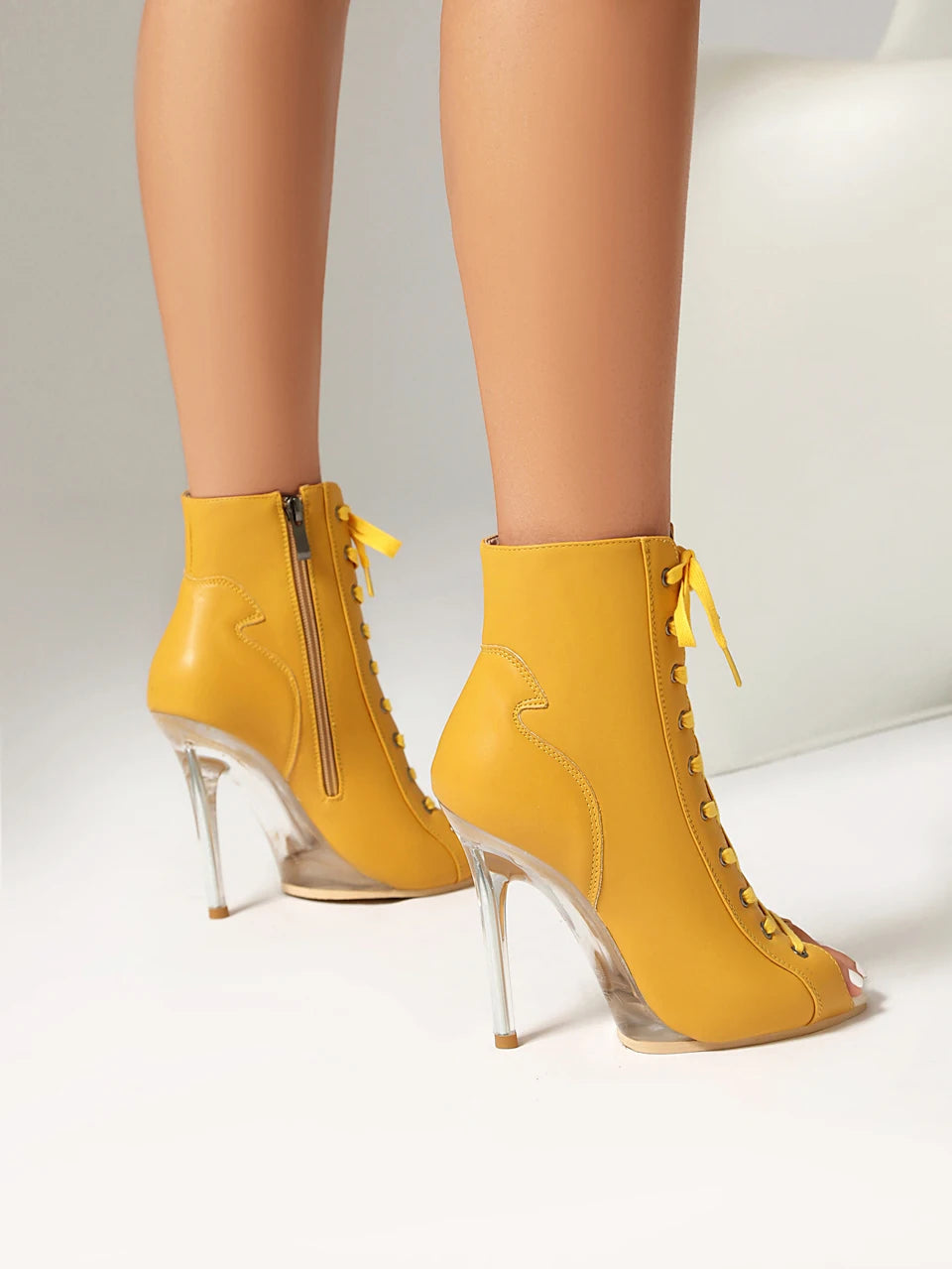 Yellow high-heeled ankle boots with clear heels on a neutral background