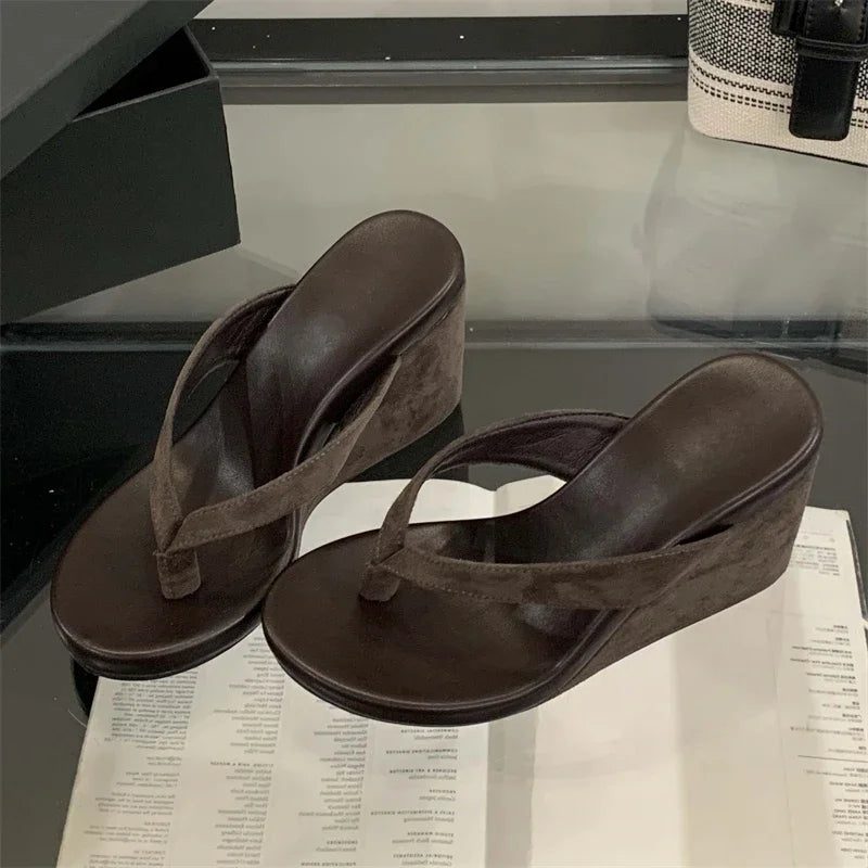 Brown wedge sandals on a reflective surface with a blurred background