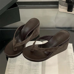 Brown wedge sandals on a reflective surface with a blurred background