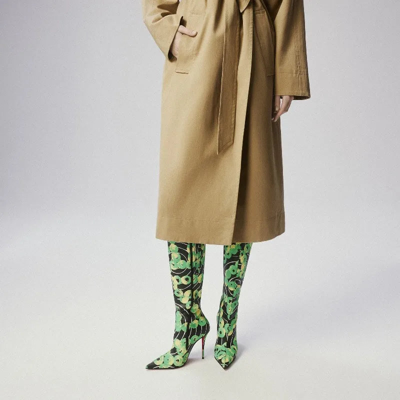 Person wearing a beige trench coat and green patterned high heels on a light gray background