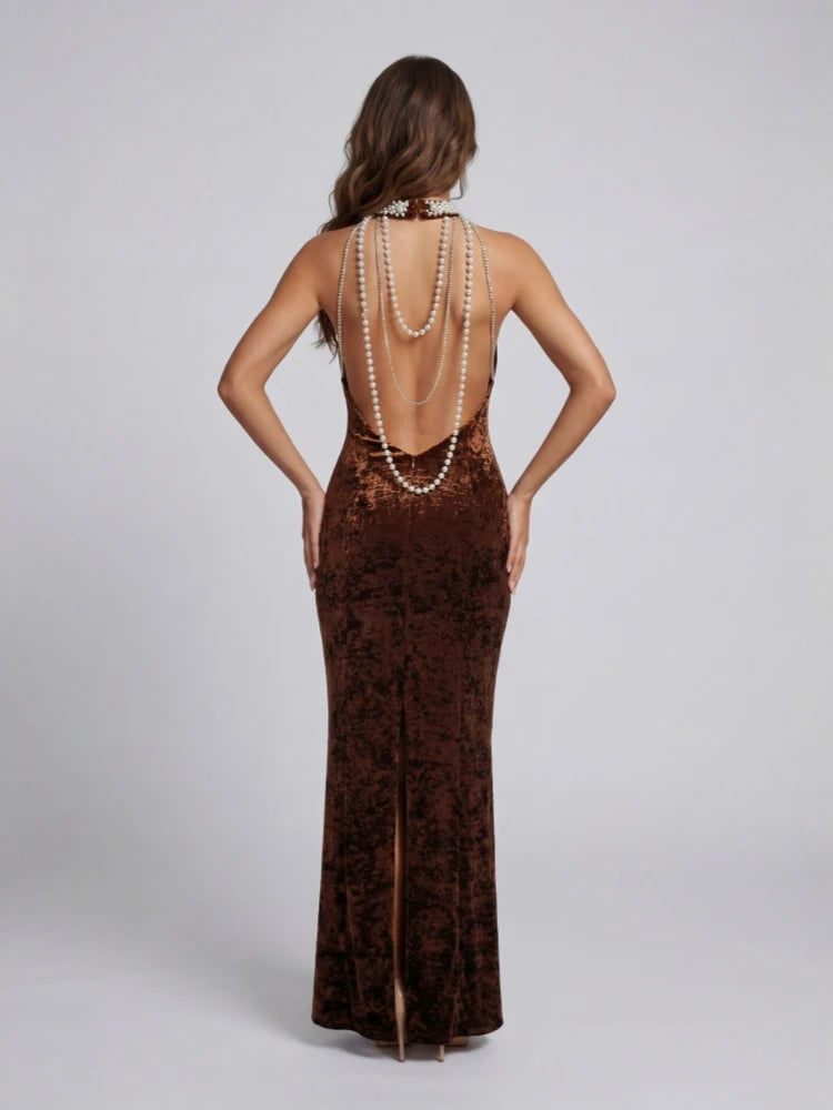 Woman wearing a brown evening gown with a high slit and pearl necklace on a light gray background