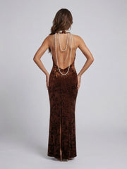 Woman wearing a brown evening gown with a high slit and pearl necklace on a light gray background