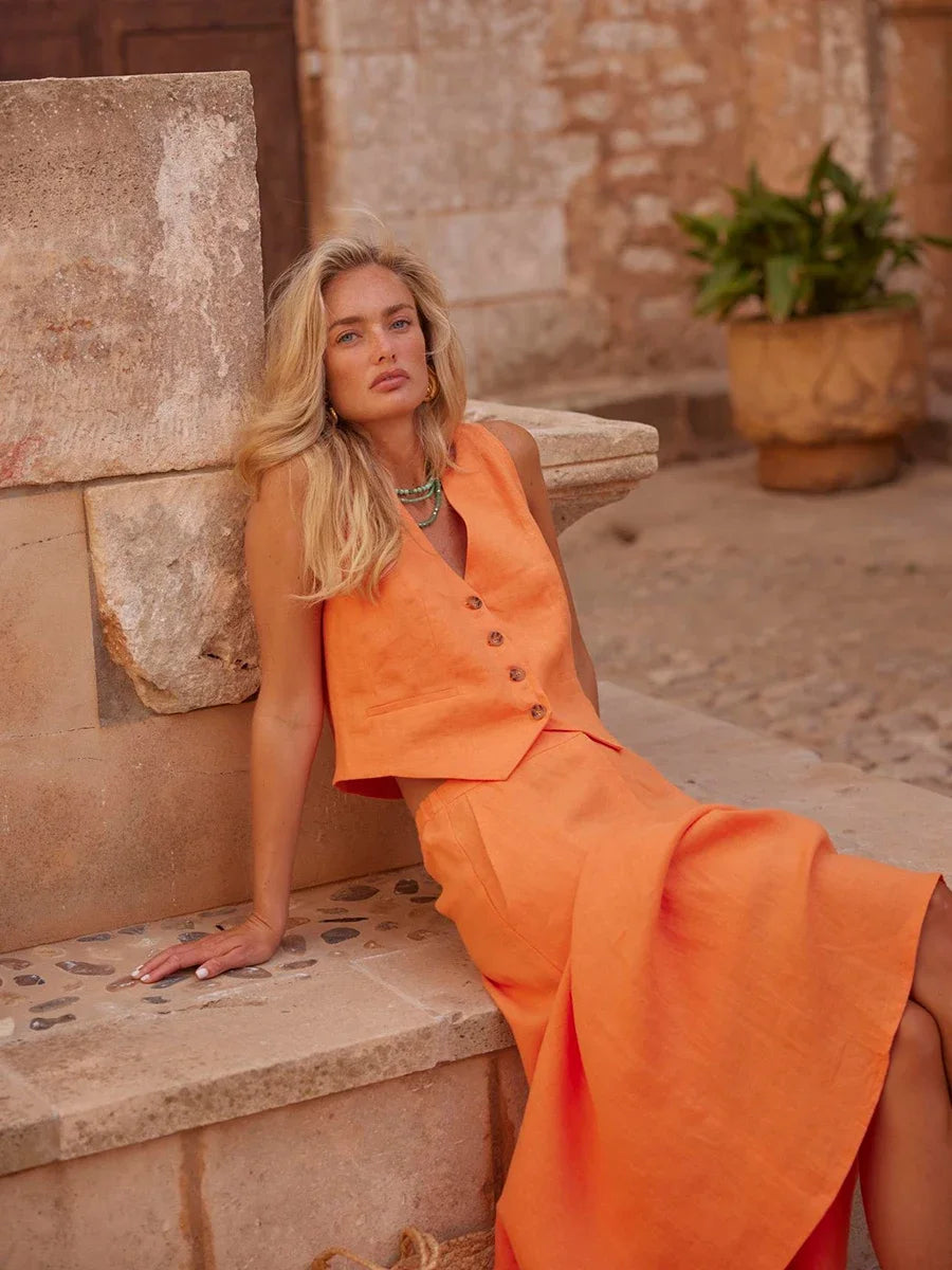 Woman in an orange dress sitting on stone steps with a stone wall and plant in the background
