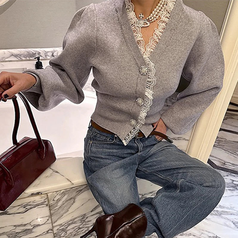 Person wearing a gray cardigan with lace trim and blue jeans, sitting on a marble floor.