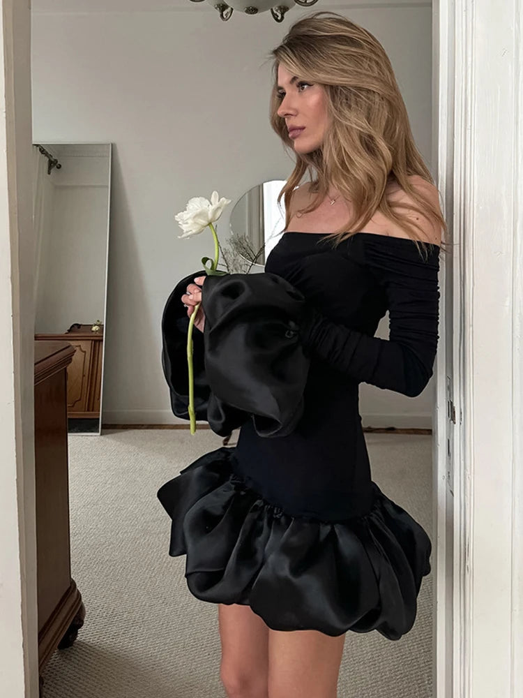 Woman in a black off-shoulder dress holding a white flower in front of a mirror.
