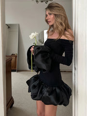 Woman in a black off-shoulder dress holding a white flower in front of a mirror.