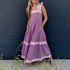 Woman wearing a pink floral dress against a dark brick wall.