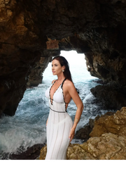 Woman in a white dress standing in a cave with ocean view