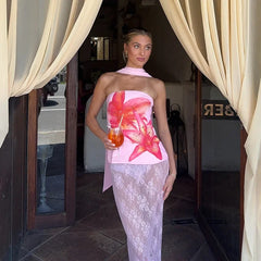 Woman in a floral dress holding a drink, standing in front of a doorway with curtains.