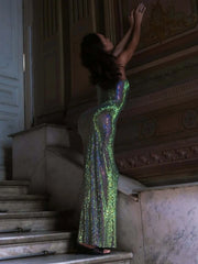 Woman in a green sequin dress standing on a staircase in an elegant interior setting.