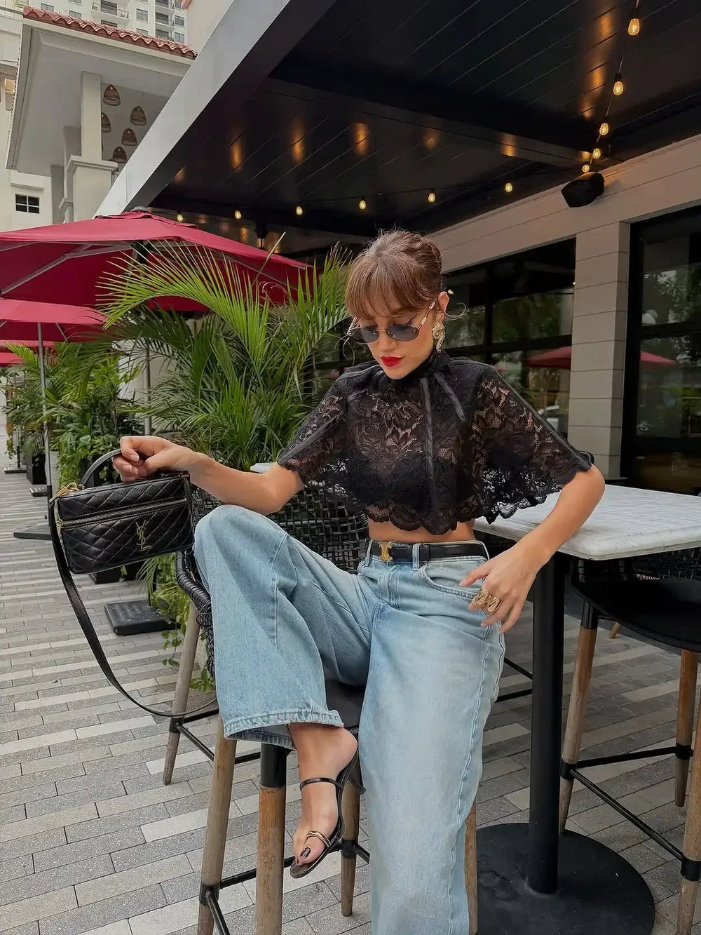 Woman sitting outdoors at a restaurant with red umbrellas and plants in the background