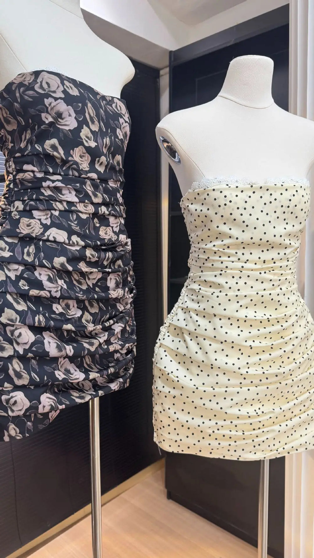 Two strapless dresses on mannequins, one with floral pattern and the other with polka dot pattern, against a dark background.