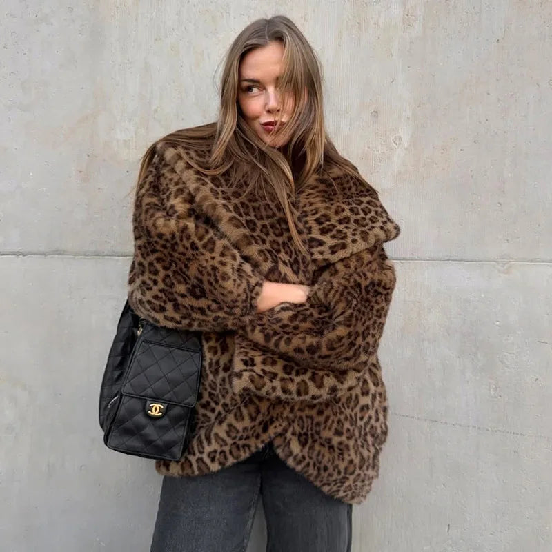 Person wearing a leopard print coat with a black quilted bag against a light-colored wall.