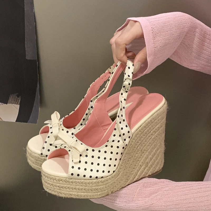 White wedge sandals with black polka dots held by a person wearing a pink sweater.