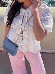Person wearing a white lace top and pink pants, holding a blue handbag.