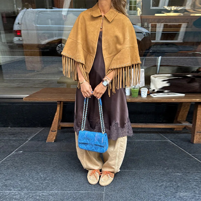 Person wearing a brown suede fringe jacket holding a blue handbag on a city street.