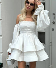 Woman wearing a white dress with ruffled sleeves in front of a gray door.