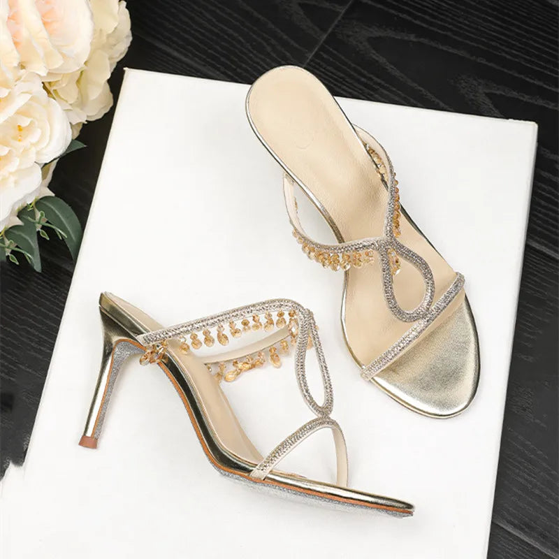 Gold high-heeled shoes with decorative straps on a white surface with flowers in the background