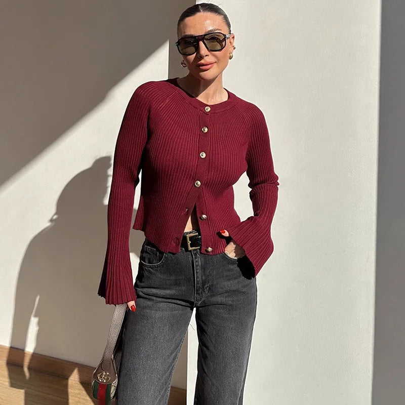 Woman wearing a red ribbed sweater and dark jeans against a light wall.
