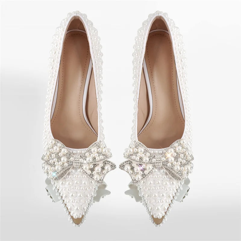 Pair of white pointed toe stiletto heels covered in pearls and a crystal bow