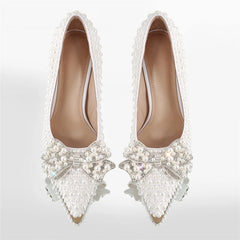 Pair of white pointed toe stiletto heels covered in pearls and a crystal bow