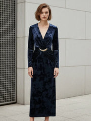 Woman wearing a dark blue velvet dress with a gold belt against a gray tiled wall.