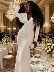 Woman in a white dress standing in an elegant banquet hall with chandeliers and tables.