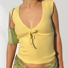 Person wearing a yellow sleeveless top with a deep neckline and green patterned pants, holding a matching green handbag.