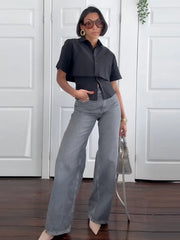 Woman wearing a black top and gray jeans standing indoors.