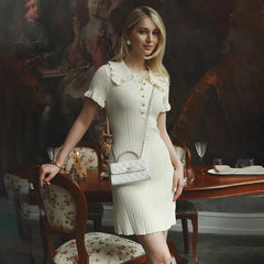 Woman in a white dress holding a handbag in a formal dining room setting