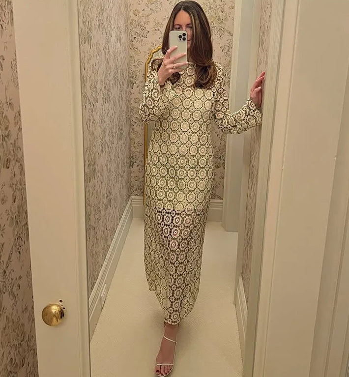 Woman taking a mirror selfie wearing a patterned dress in a room with floral wallpaper.