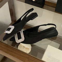 Black pointed-toe shoes with decorative buckles on a reflective surface