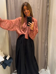 Woman taking a mirror selfie wearing a pink blouse and black pants.