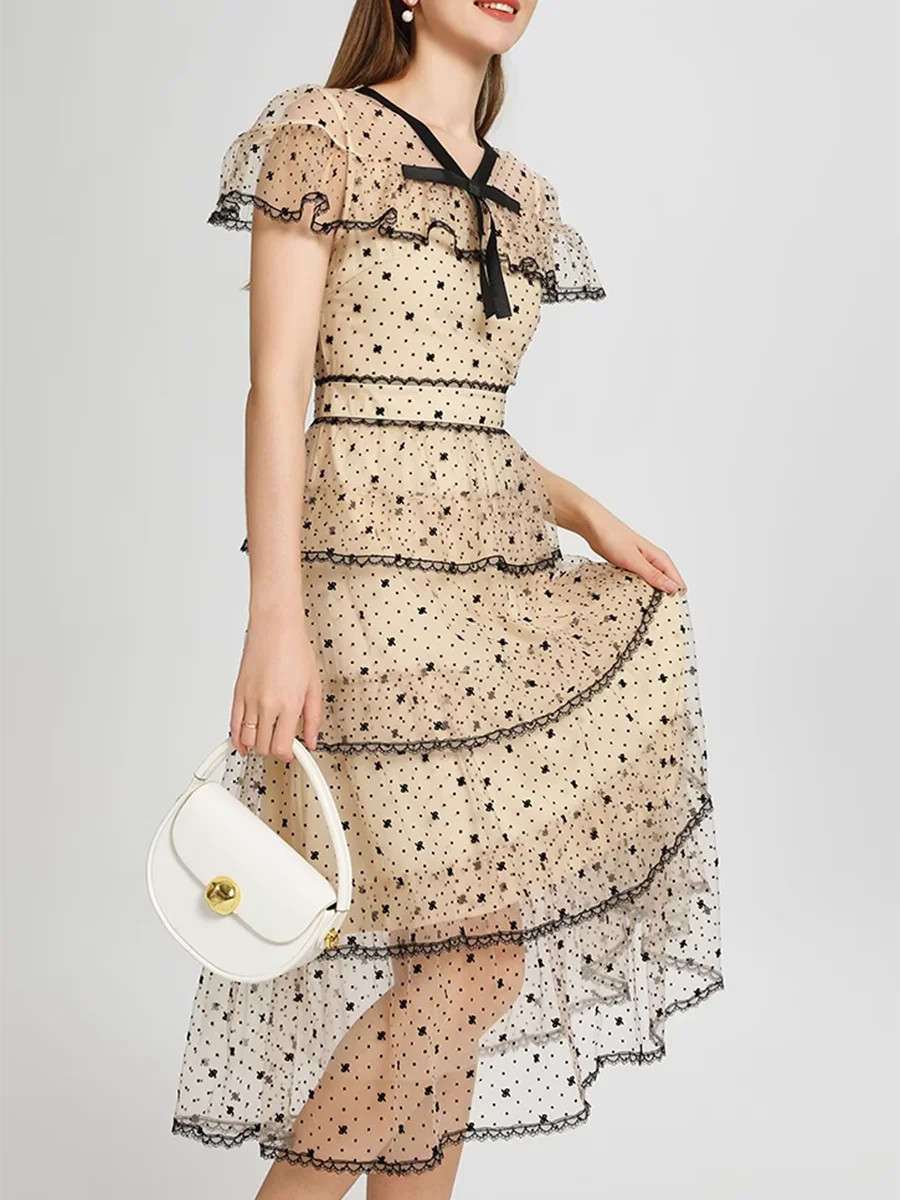 Woman wearing a beige floral dress with black details, holding a white handbag on a light gray background