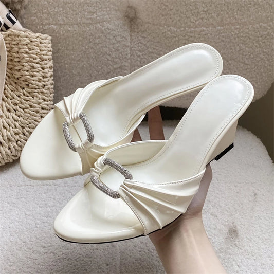 White patent leather wedge slippers with crystal buckle and pleated detail.