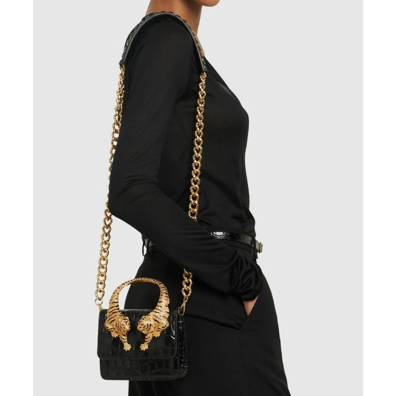 Side view of a black crocodile effect top handle bag with gold tiger sculptures and chain strap