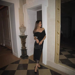 Woman in a black dress standing in a room with checkered floor and decorative wall.